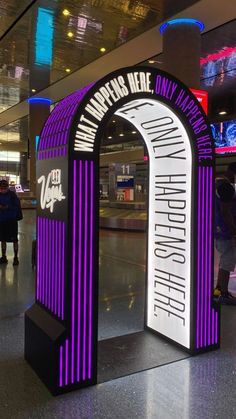 the entrance to an airport with purple and white signage on it's sides, along with people walking by