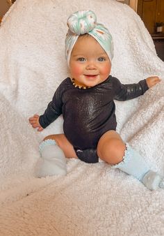 a baby sitting on top of a white blanket wearing a black shirt and blue socks