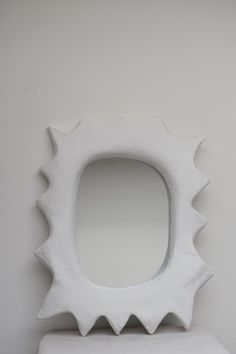 a white sculpture sitting on top of a table next to a wall with a mirror in the shape of a sun