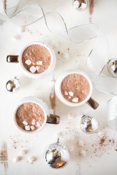 two mugs of hot chocolate with marshmallows and white ribbon on the side