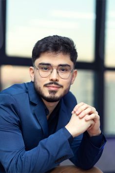 a man wearing glasses sitting at a table with his hand on his chin and looking off to the side