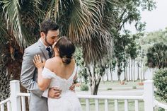 a bride and groom standing on a porch next to palm trees looking at each other