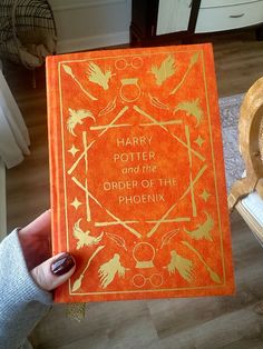 a person holding up an orange book with harry potter and the order of the phoenixix written on it