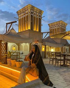 a woman sitting on top of a stone bench next to a tall building at night