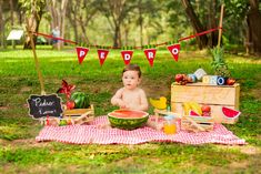 a baby is sitting on a blanket with watermelon in front of him and other food