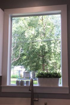 a kitchen sink under a large window with trees outside