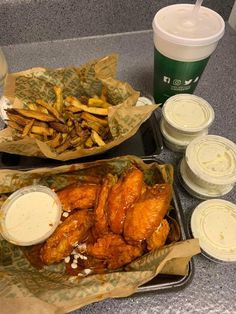 two trays filled with chicken wings and french fries next to cups of drinks on a counter