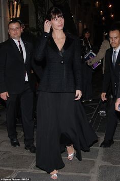 a woman in a long black dress is talking on her cell phone while walking down the street