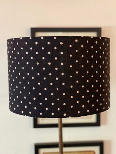 a black and white polka dot lampshade on a table with framed pictures in the background