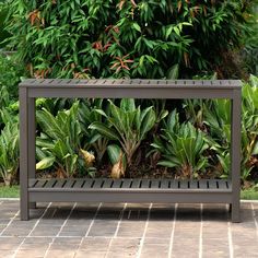 a metal bench sitting on top of a brick floor next to green plants and bushes