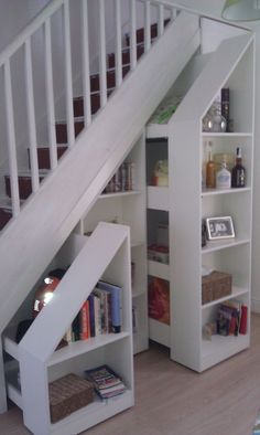 an under the stairs bookcase with books and drinks in it is next to a stair case