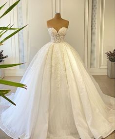 a white wedding dress on display in front of a wall with potted plants behind it