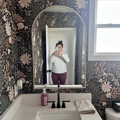 a woman taking a selfie in front of a bathroom mirror with flowers on the wall