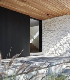 an exterior view of a modern house with stone walls and wood ceiling, grass in the foreground