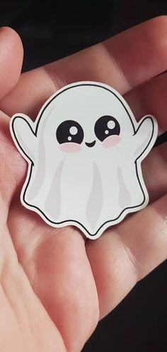 a hand holding a white sticker with a ghost on it's face and eyes