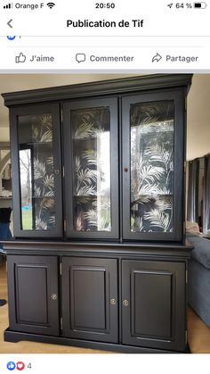 a black china cabinet with glass doors on the top and bottom, in front of a couch