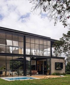 a modern house with large windows and a pool in the front yard, surrounded by green grass