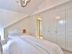 a white bed sitting under a chandelier in a bedroom next to closets