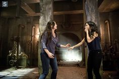 two women are standing in an old factory talking to each other and holding hands with one another