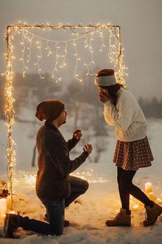 two people kneeling down in the snow with lights strung up around them and one person holding a cell phone