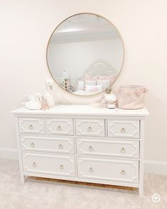 a white dresser topped with a round mirror and stuffed animals on top of it's drawers