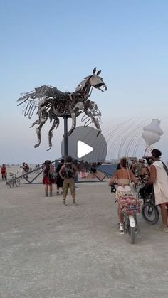 people are standing around in front of a large metal horse on the beach with bicycles