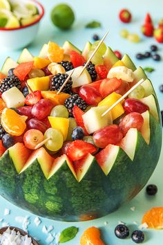 a watermelon bowl filled with fruit and skewers