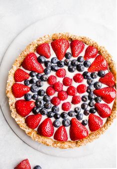 a pie topped with strawberries and blueberries on top of a white plate next to berries