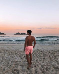 a man standing on top of a sandy beach next to the ocean in pink trunks