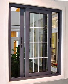 an open window on the side of a building with white trim and black frame, in front of a green plant