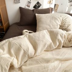 an unmade bed with pillows and blankets on top of it in front of a bookshelf