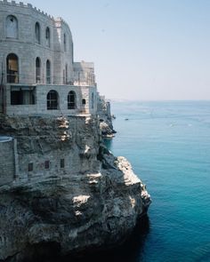 an old building sitting on top of a cliff next to the ocean with blue water