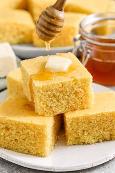 a white plate topped with pieces of cornbread next to a jar of honey on the side