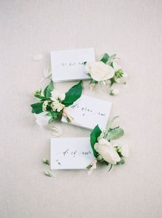 three place cards with flowers and greenery on the top are placed next to each other