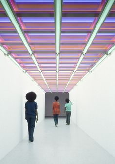 three people walking down a white hallway with colorful lights on the ceiling and flooring