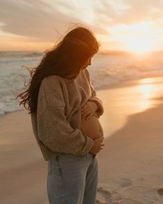 a woman holding a baby on the beach at sunset