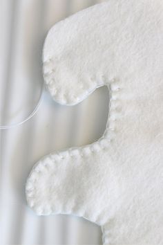 a close up of a white teddy bear made out of felt on a bed sheet