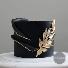 a black hat with gold leaf decoration on it's side, sitting on top of a white table