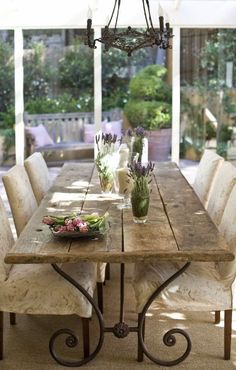 a wooden table with white chairs and flowers in vases on top of it next to a chandelier