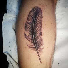 a black and white photo of a tattoo with a feather on it's leg