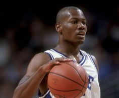 a man holding a basketball in his right hand and wearing a white jersey with blue lettering on it