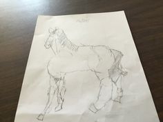 a drawing of a horse standing on top of a wooden table next to a piece of paper