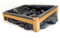 the dog bed is made from wood and has a grey blanket on top of it