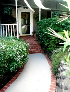 the front door of a house with plants and bushes around it, along with a walkway