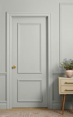 an empty room with a white door and some flowers on a small table next to it