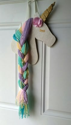 a unicorn head hanging from the side of a white door with multicolored yarn