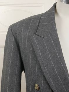 This handsome gray pinstripe double-breasted blazer has peak lapels and padded shoulders, and closes in the front with one faux tortoiseshell button (six in total show on the front). Three buttons also decorate each sleeve edge. The German jacket has three pockets on the front, and is lined in a silvery gray satin viscose fabric. Brand: International Style (Germany) Size: 40 US/UK Material: 70% wool, 30% polyester Condition: Excellent (clean, soft, and supple, with no stains, tears, wear spots, Pinstripe Business Outerwear For Winter, Winter Pinstripe Formal Outerwear, Winter Striped Single Breasted Blazer, Winter Striped Single-breasted Blazer, Winter Formal Pinstripe Outerwear, Fitted Pinstripe Outerwear For Semi-formal Occasions, Pinstripe Outerwear For Winter Office, Tailored Pinstripe Winter Outerwear, Double-breasted Pinstripe Blazer For Formal Occasions