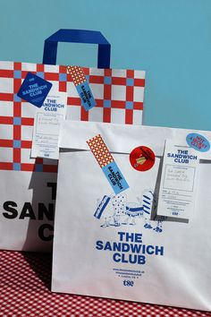 two paper bags sitting on top of a red and white checkered cloth covered table