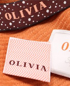 an orange sweater with the name olivia on it next to a white and black label