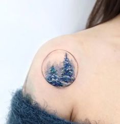 a small snow globe tattoo on the left upper arm, with pine trees in it